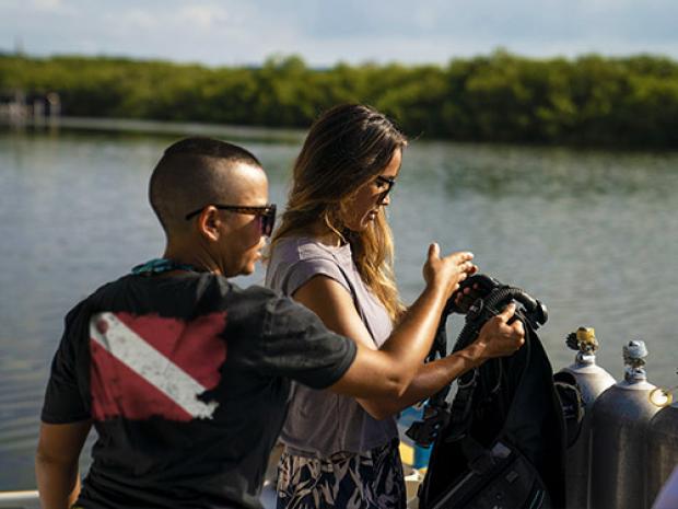 A divemaster helps a diver with their gear