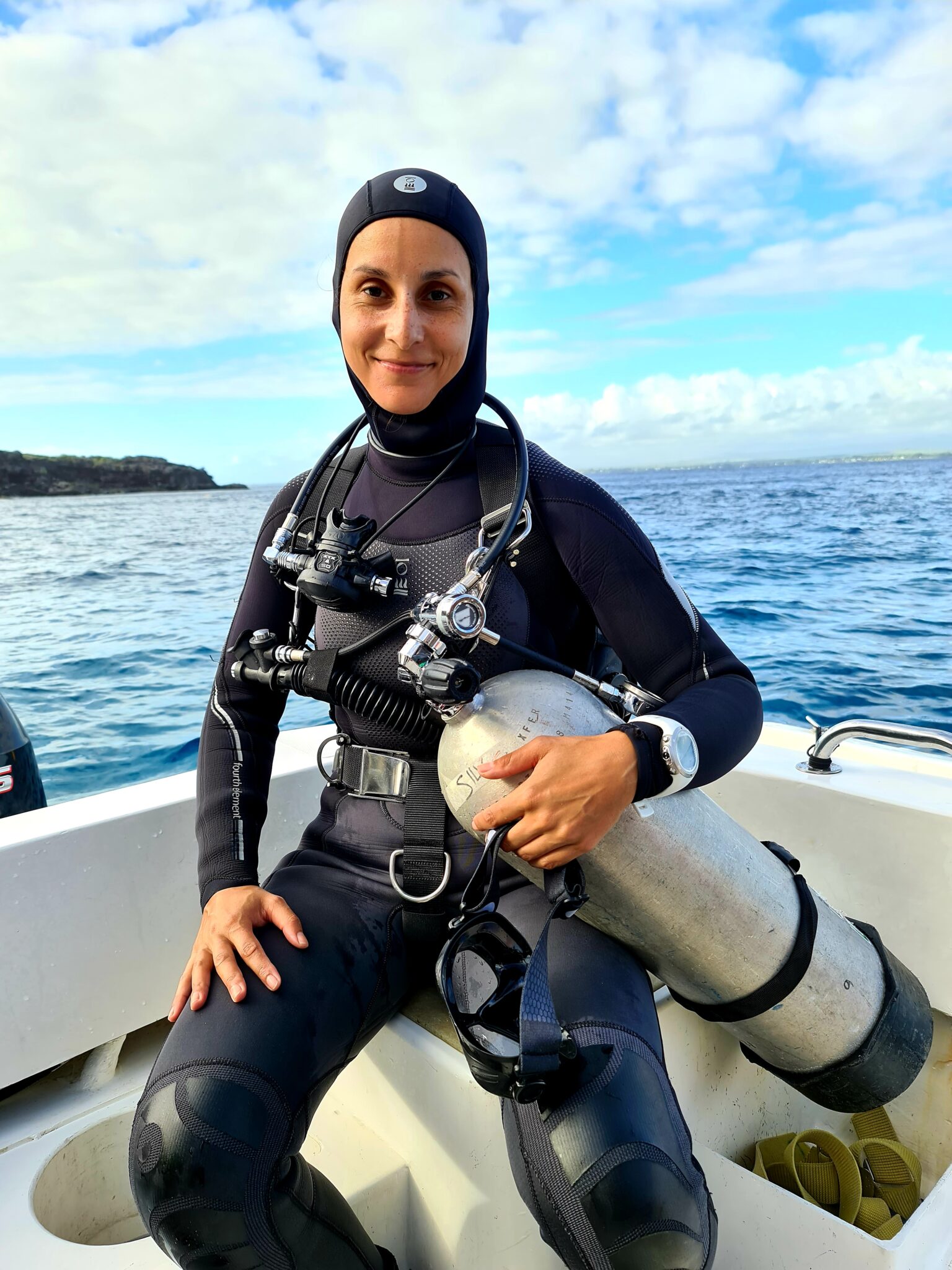 A female diver sits on the bow of a boat, smiling as she waits to go underwater.