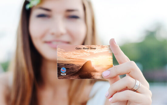 person holding open water diver certification card with shark fin sunset image