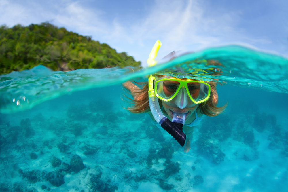 a girl with a yellow mask snorkelling in blue water