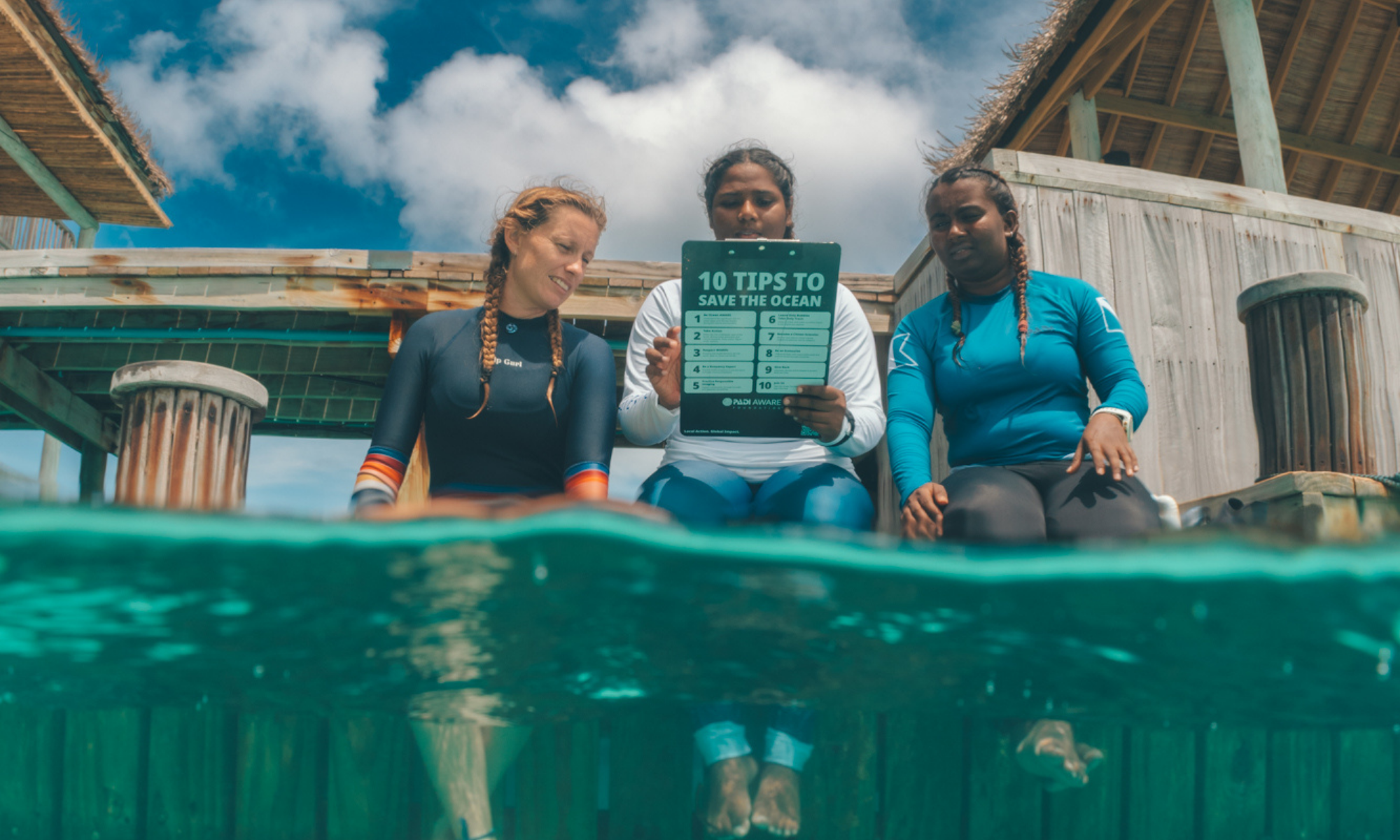 Three girls sit on a dock reading tips to save the ocean