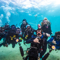 A group photo of several enthusiastic divers underwater with coral restoration trees in the background