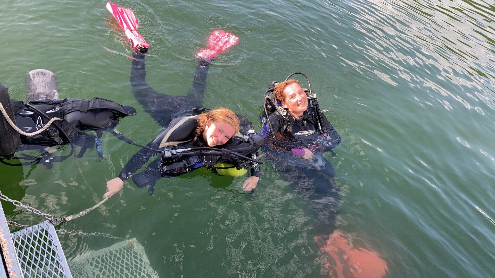 DIvers Cheyenne and Sarah rest at the surface smiling at the camera.
