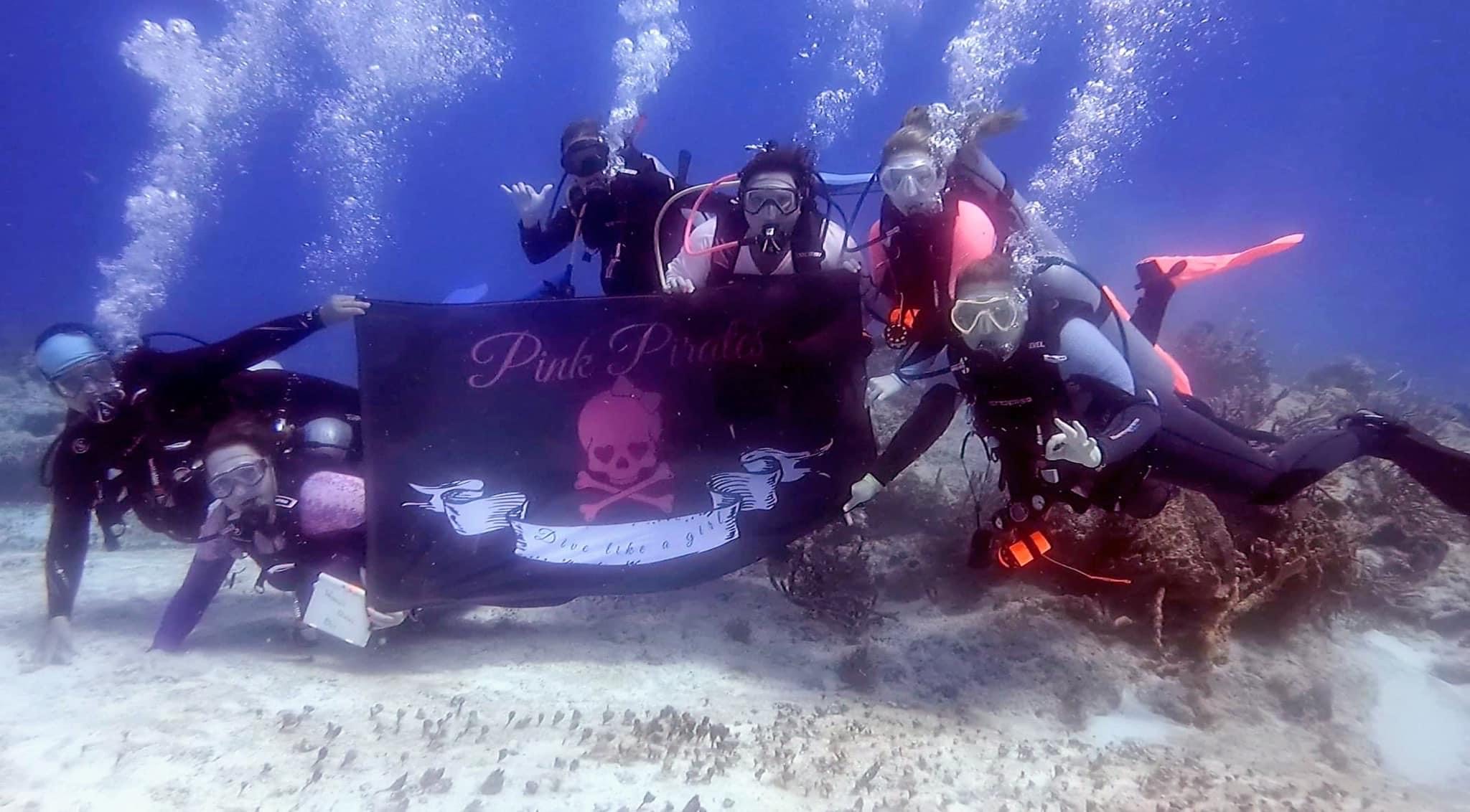 All-female divemaster class holding a Pink Pirate flag underwater