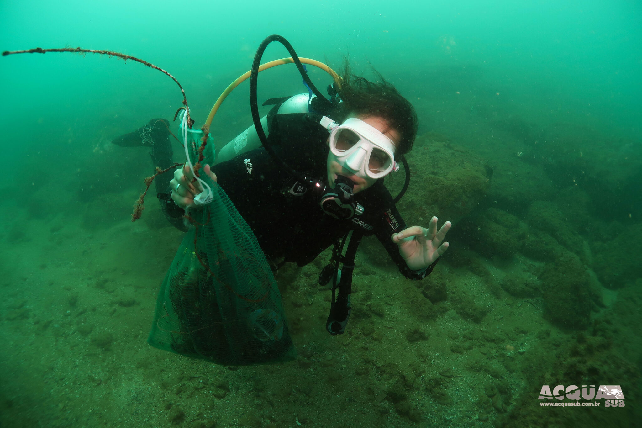 A diver gives the "okay" signal while holding a bag of debris collected from the ocean floor.