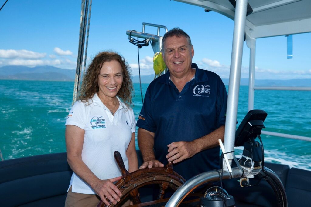 Taryn stands next to Perry near the wheel on their sailing vessel, driving over the great barrier reef