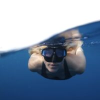 A split image of a woman freediving in the ocean, coming at the camera head on.