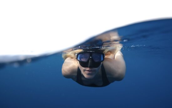 A split image of a woman freediving in the ocean, coming at the camera head on.