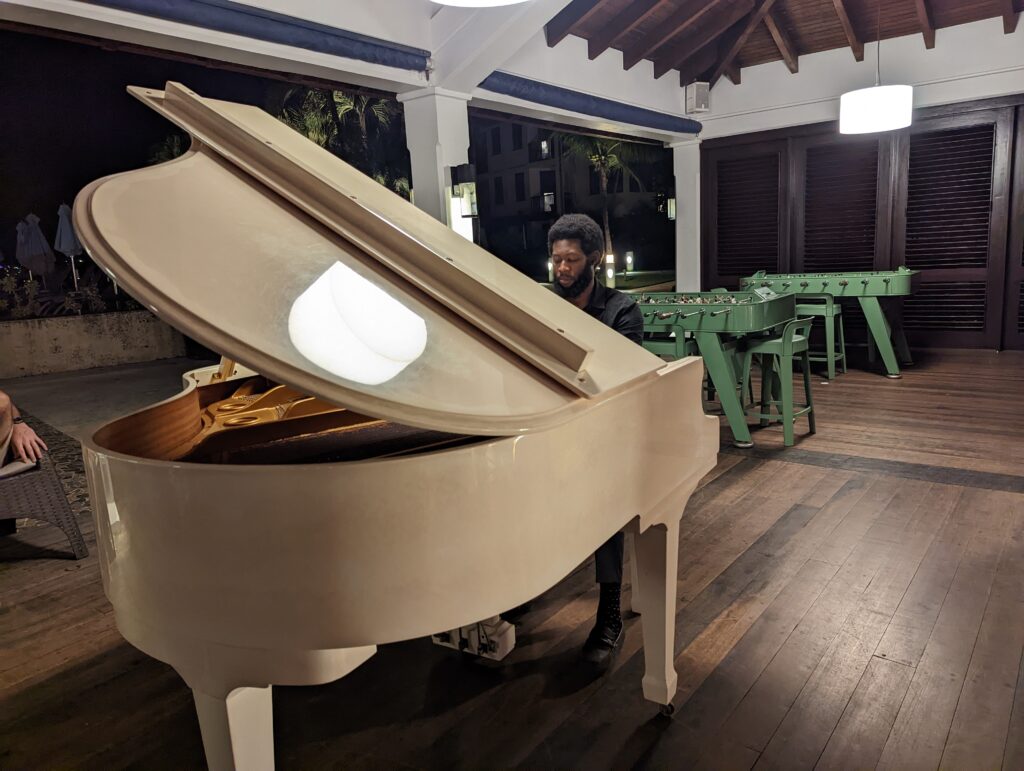 A man plays on a white grand piano in an open-air salon at Sandals Resorts.
