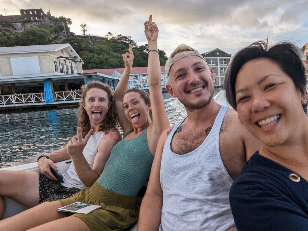Four friends take a selfie on the back of a boat leaving Sandals Resorts. Their hands are up and tongues out.