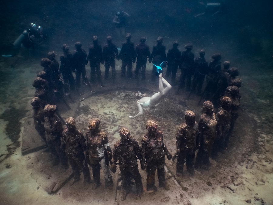 A freediver floats in the middle of a circle of sculptures underwater.