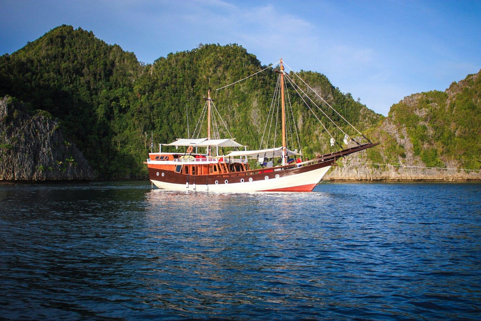 a traditional wooden boat floats in front of an island in Indonesia