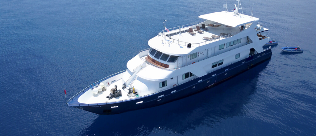 A scuba liveaboard boat on the water with two zodiac boats behind it