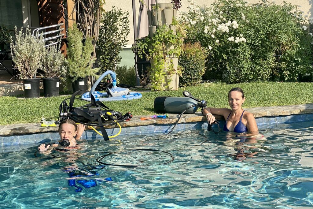 Two divers set their gear on the side of a pool.