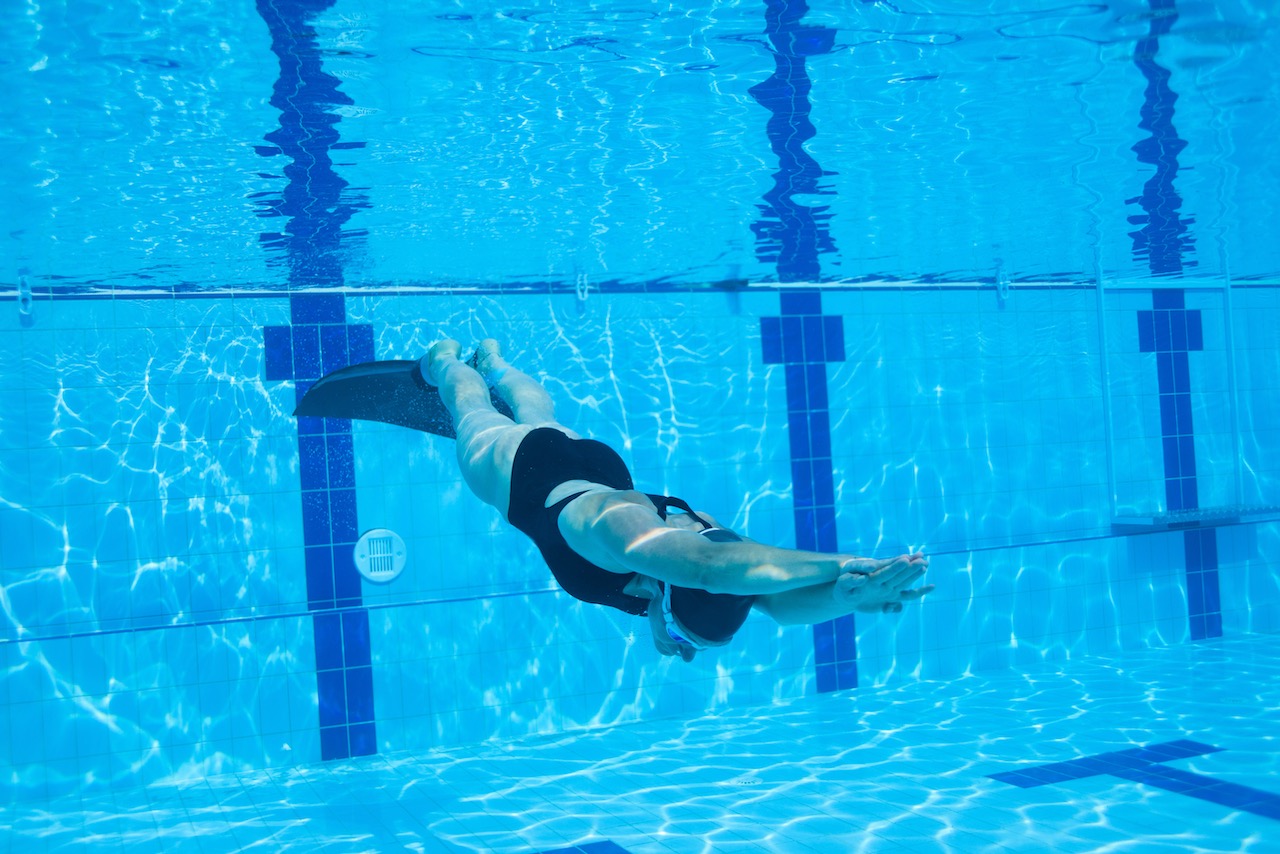 Female freediver with monofin swimming underwater in swimming pool, practicing dynamic apnea
