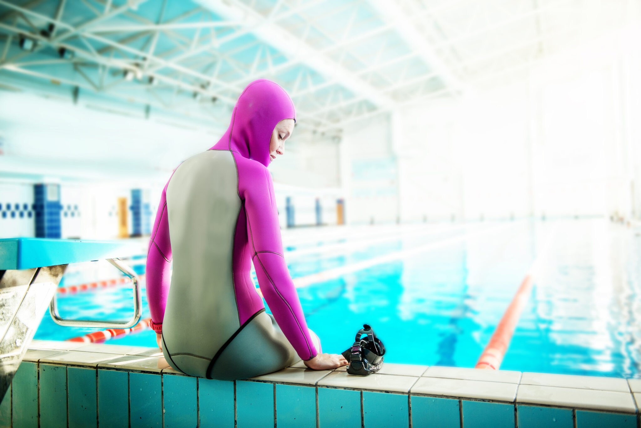 A woman sits by the side of a pool in freediving gear. She is going to practice dynamic apnea.