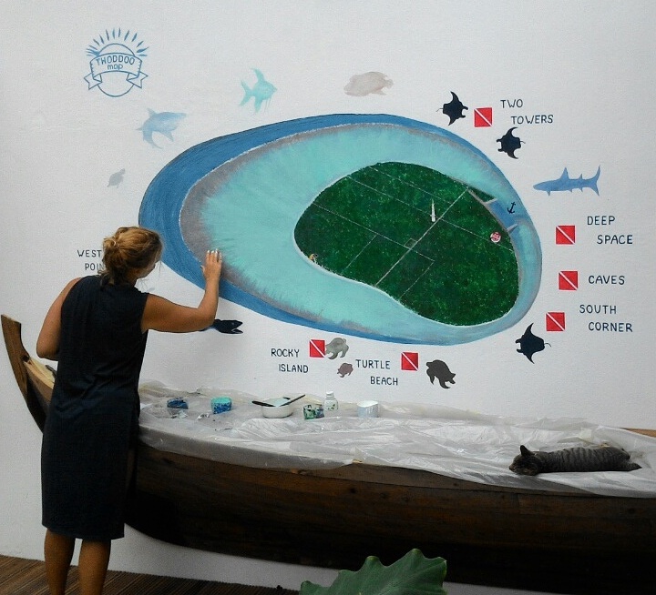 A woman paints a mural showing an island in the Maldives and its surrounding dive sites