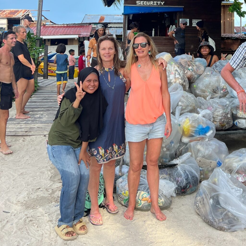 three women stand in front of a pile of garbage bags on a beach in Borneo
