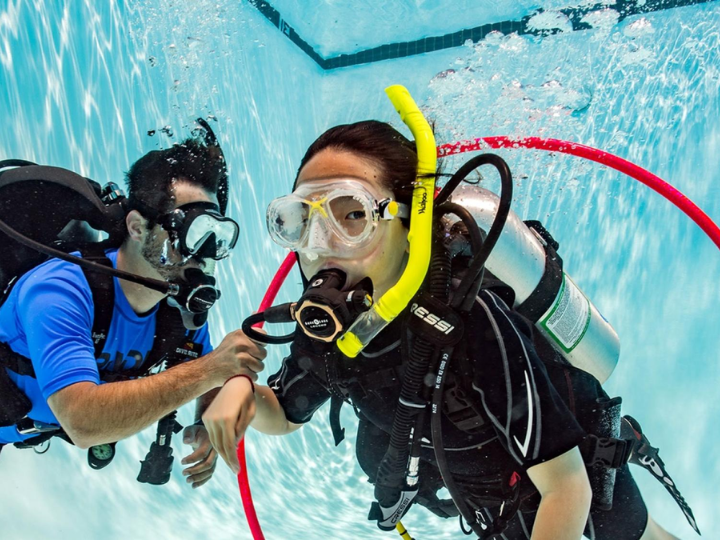 a young scuba diver swims through a hoop in full dive gear in a swimming pool. The hoop is being held by a scuba instructor and this exercise is part of the Seal Team training for young divers.