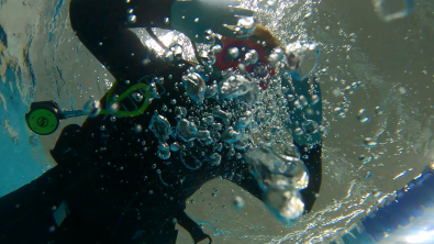a woman looks at an underwater camera and blows bubbles