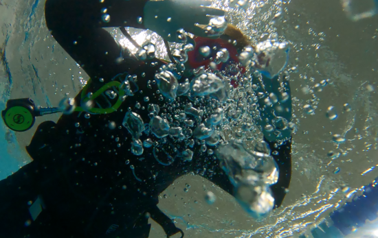 a woman looks at an underwater camera and blows bubbles