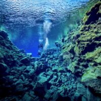two divers float underwater together in Silfra, Iceland after learning to scuba dive