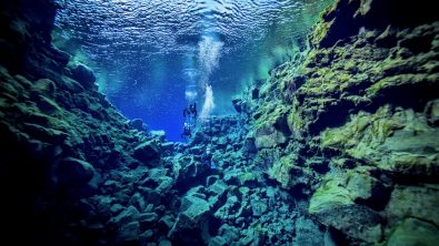 two divers float underwater together in Silfra, Iceland after learning to scuba dive