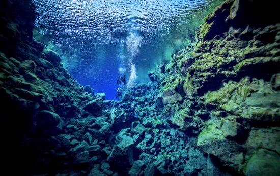 two divers float underwater together in Silfra, Iceland after learning to scuba dive