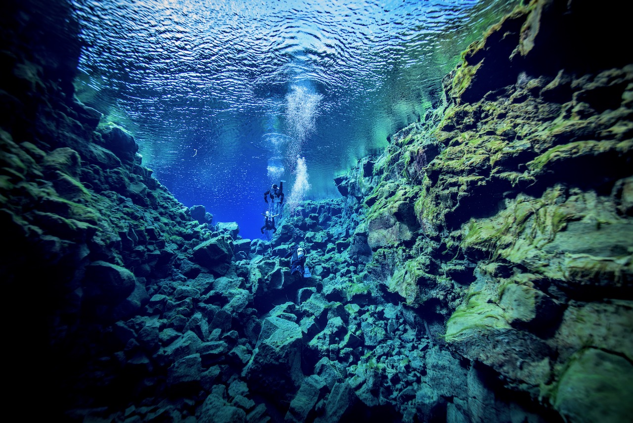 two divers float underwater together in Silfra, Iceland after learning to scuba dive