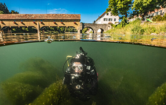 In this split shot, we see a scuba diver in a river in Germany with historical buildings above