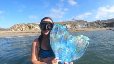 a mermaid shows her monofin to the camera above the surface