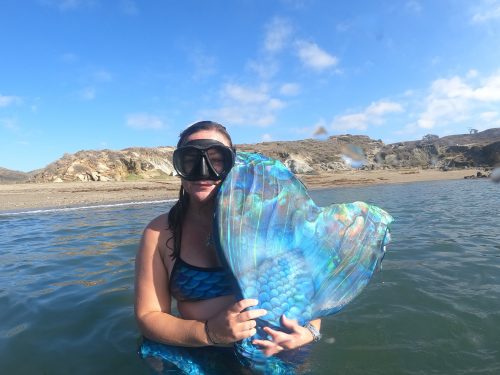 a mermaid shows her monofin to the camera above the surface