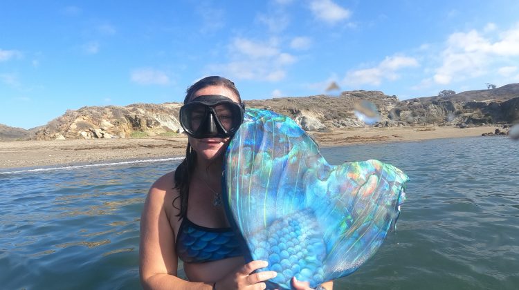 a mermaid shows her monofin to the camera above the surface