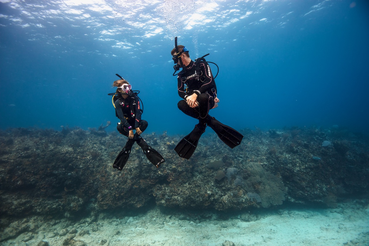 two padi peak performance buoyancy divers practice hovering underwater in the ocean