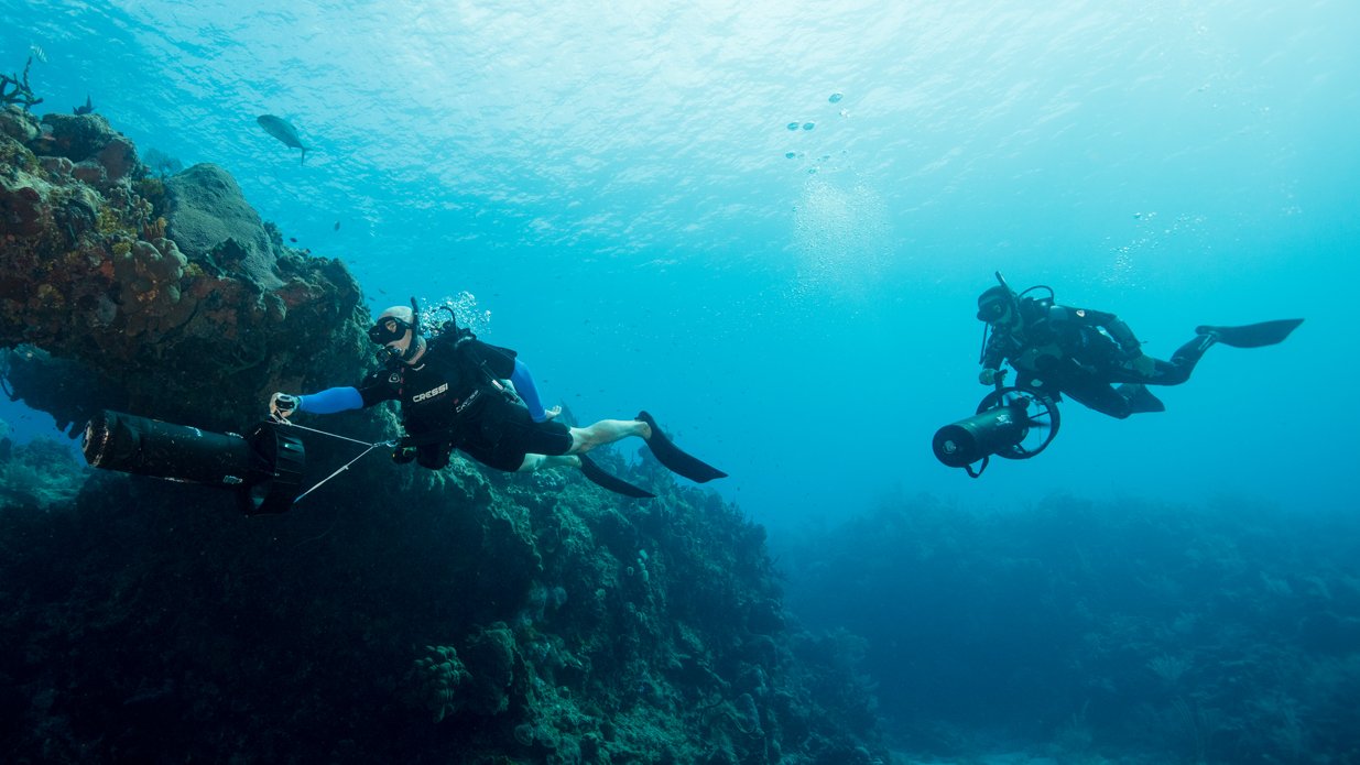two divers use dpvs to explore a coral reef