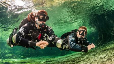 two scuba divers explore the underwater world using a sidemount configuration for their scuba tanks