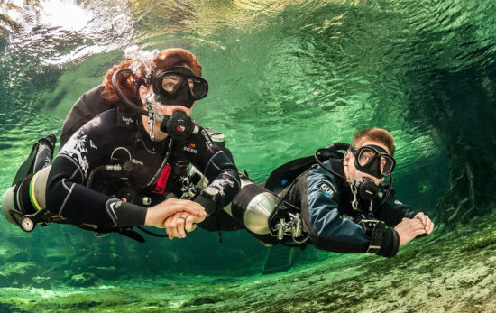 two scuba divers explore the underwater world using a sidemount configuration for their scuba tanks