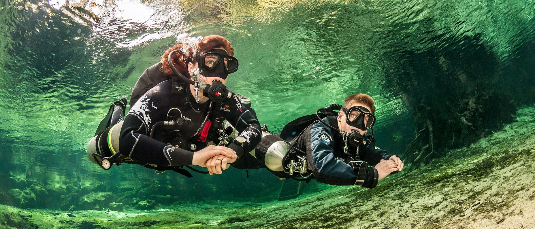 two scuba divers explore the underwater world using a sidemount configuration for their scuba tanks