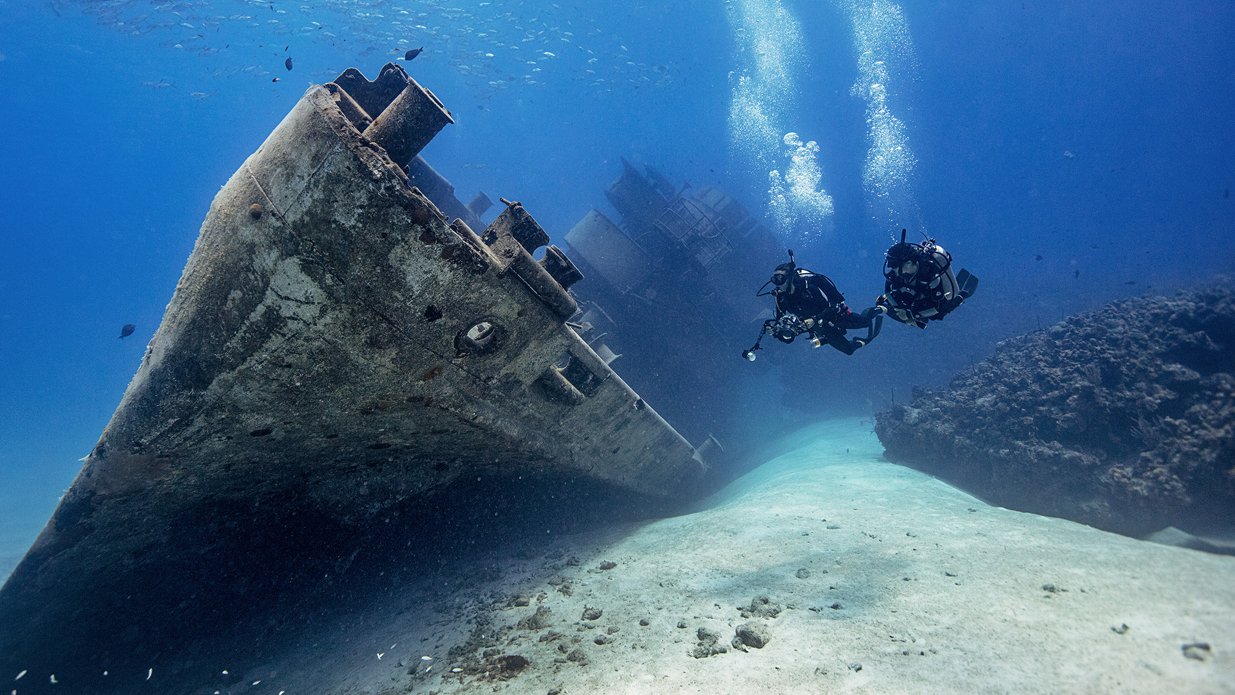 divers exploring a wreck on a sandy bottom