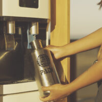 a woman fills up a padi water bottle at a water fountain in a padi eco center