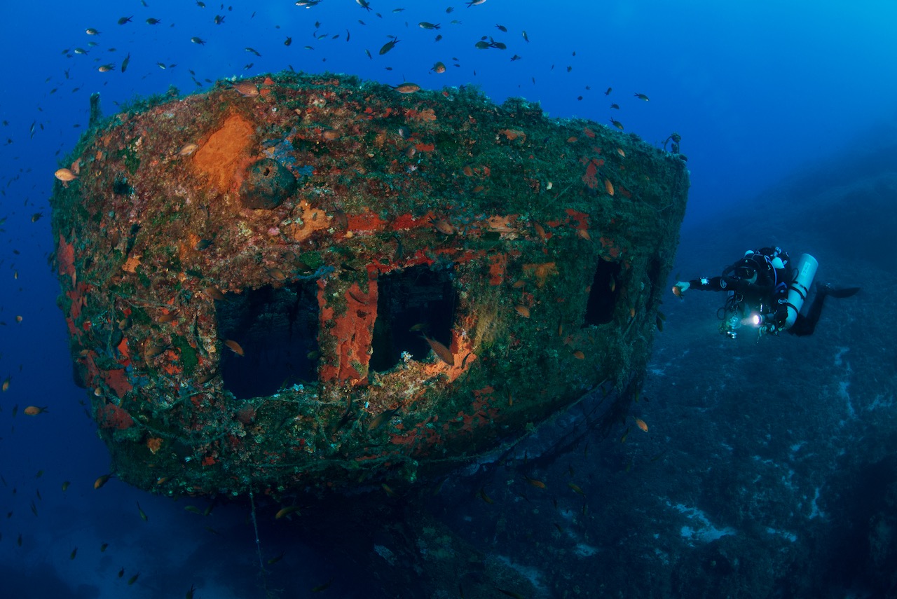 A technical diver floats past a coral-encrusted shipwreck in Greece