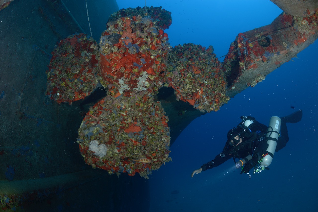 A technical diver poses next to a propeller of a large shipwreck in Greece