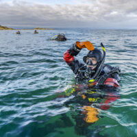 A scuba diver gives the okay symbol at the surface of the ocean. The okay symbol is when a diver touches the top of their head with their hand forming an 'o' with their head, shoulder, arm and hand.