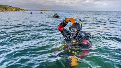 A scuba diver gives the okay symbol at the surface of the ocean. The okay symbol is when a diver touches the top of their head with their hand forming an 'o' with their head, shoulder, arm and hand.
