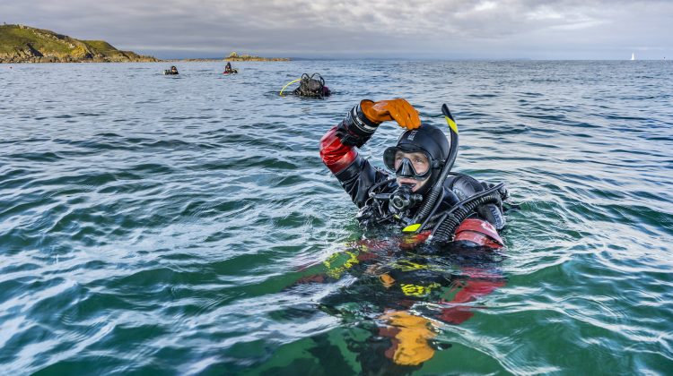A scuba diver gives the okay symbol at the surface of the ocean. The okay symbol is when a diver touches the top of their head with their hand forming an 'o' with their head, shoulder, arm and hand.