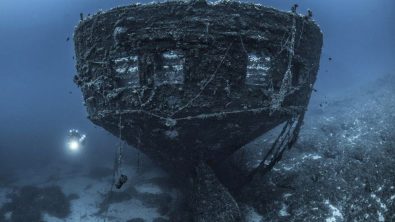 a technical diver explores the stern of a sunken ship in Greece
