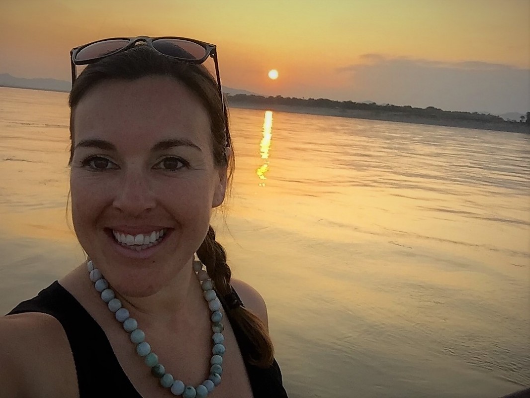 A woman (Danna Moore) takes a selfie in front of a sunset over the ocean