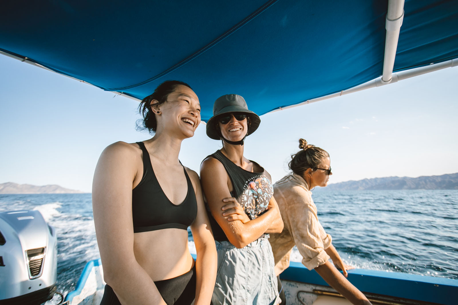 three freedivers on a boat look for signs of mobula rays in the water