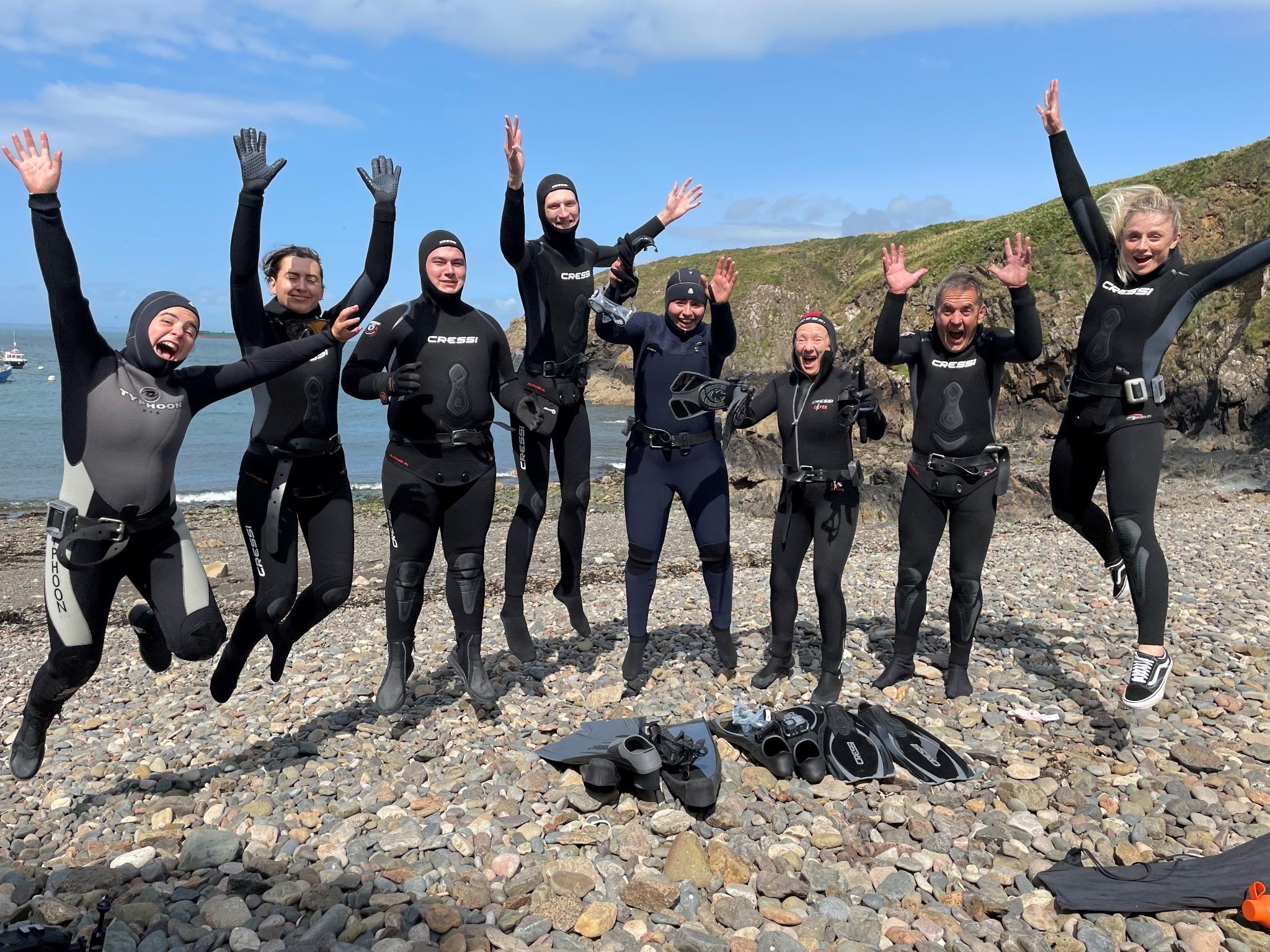 A group of divers jump in unison on a beach after a dive