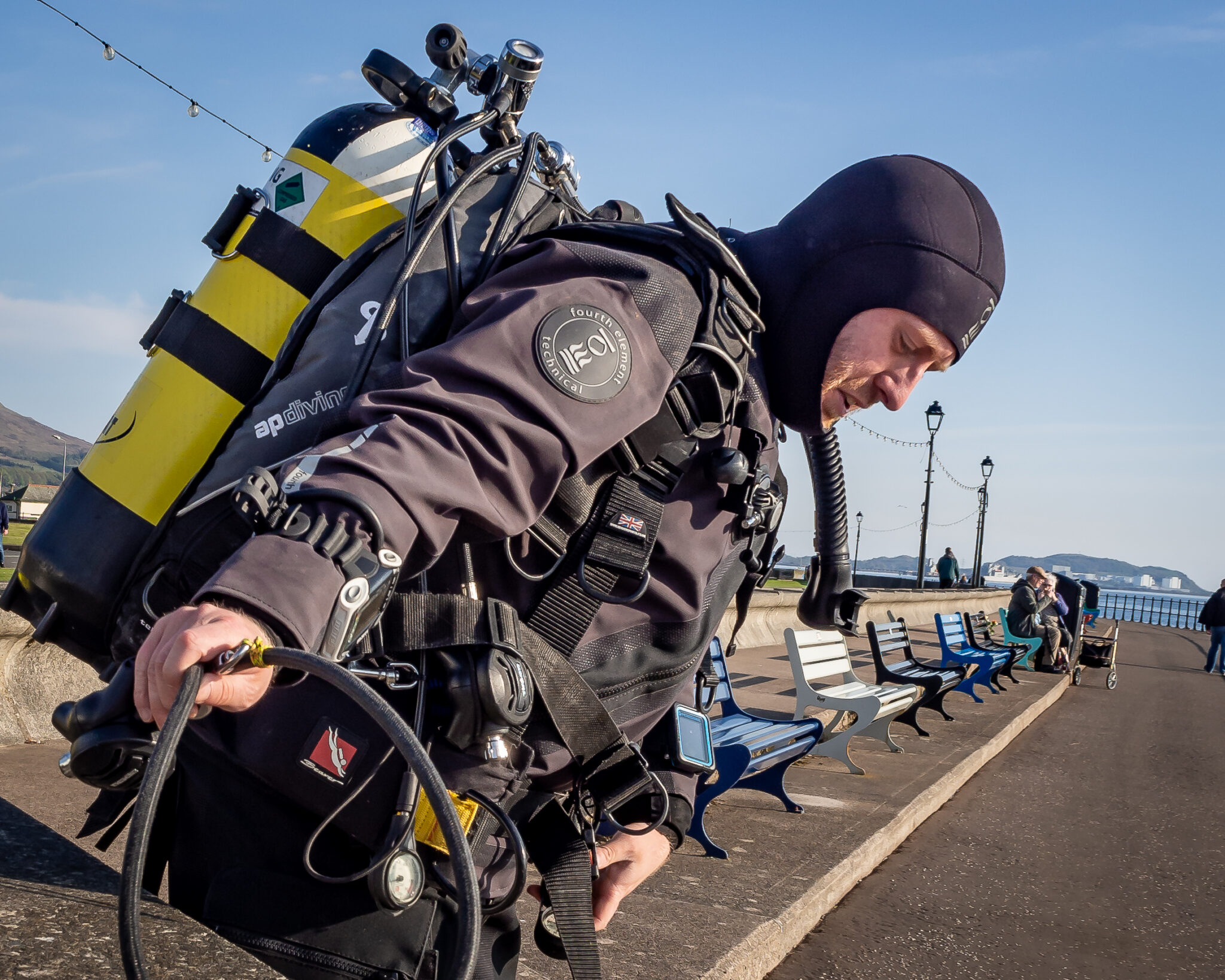 A diver gets ready to enter the water in Scotland. He is wearing a dry suit and a neoprene hood.